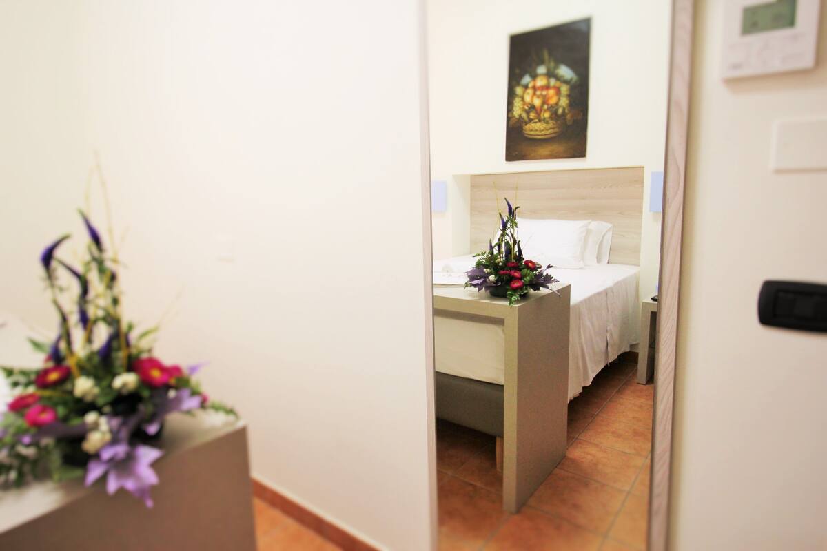 Une chambre d’hôtel avec un lit, une table de chevet agrémentée d’un arrangement floral et un tableau au mur.