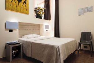 Habitación de hotel ordenada con una cama doble, mesitas de noche, un escritorio con teléfono, una silla y un televisor montado en la pared.