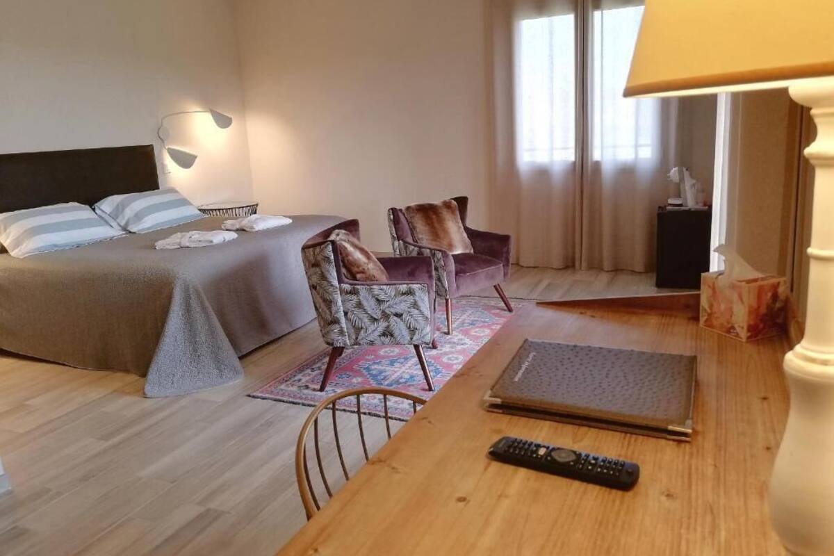 A hotel room with a bed, a desk, a chair, a lamp, and a window with curtains.