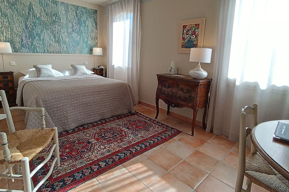 A bedroom with a bed, bedside tables, a chair, a rug, and a painting on the wall.