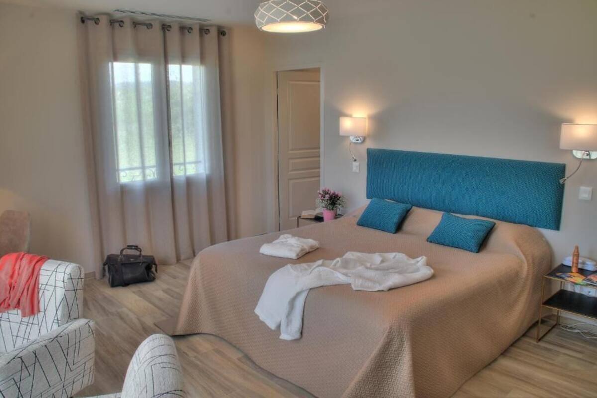 A hotel room with a bed, a chair, a nightstand, a lamp, and a window with curtains.