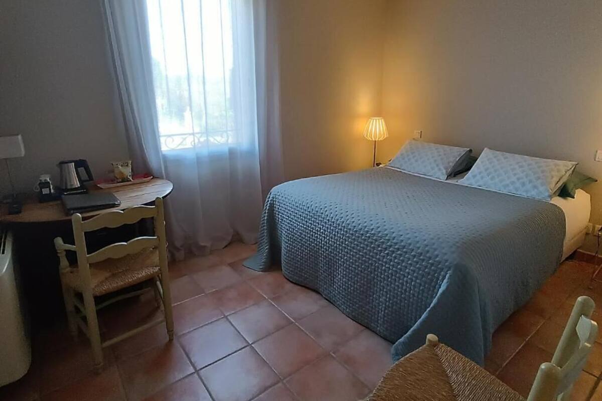 A bedroom with a bed, a desk, a chair, a lamp, and a window with curtains.
