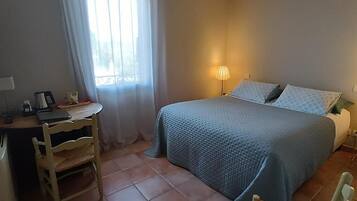 A bedroom with a bed, a desk, a chair, a lamp, and a window with curtains.