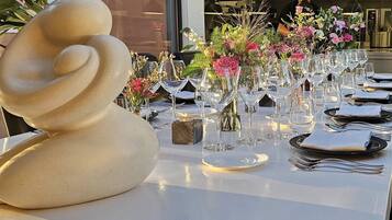 Una mesa de comedor dispuesta con varias copas de vino, platos y cubiertos, con una escultura decorativa a la izquierda.