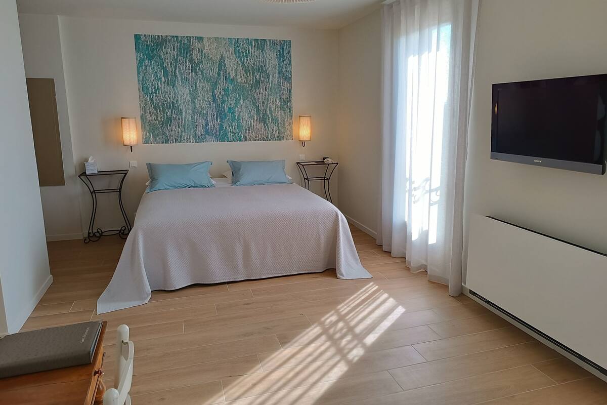 A hotel room with a bed, two bedside tables, a wall-mounted TV, and a large abstract painting.