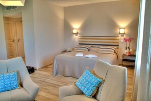 A hotel room with a bed, two armchairs, a nightstand, and a door.