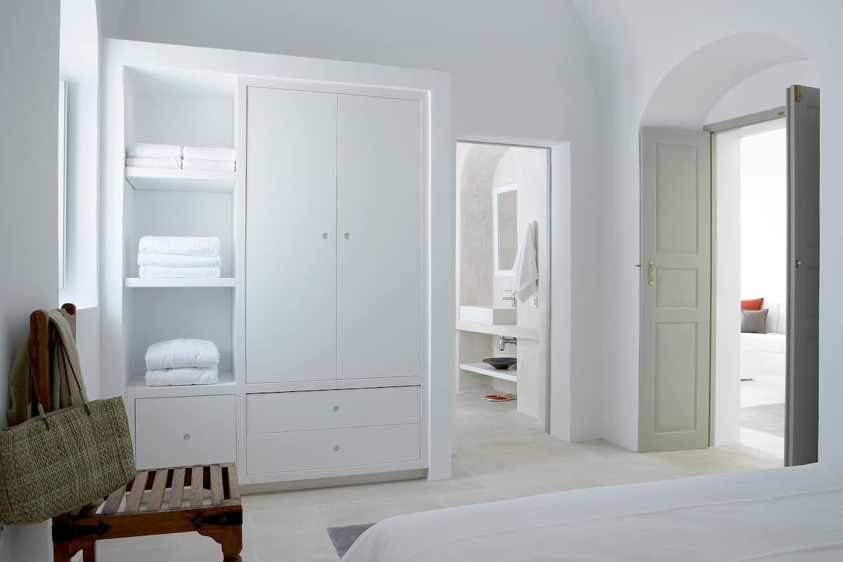 Une chambre avec une grande armoire blanche, un banc en bois et un lit.