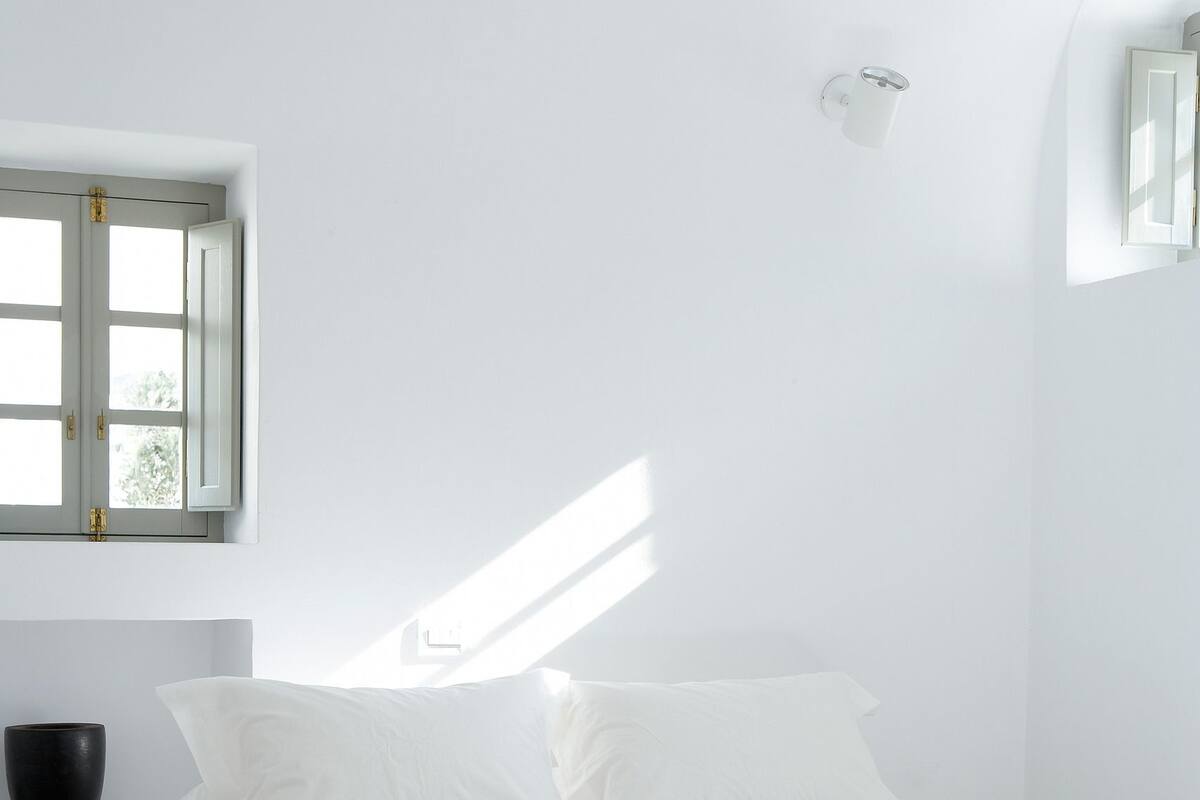 Une chambre à coucher au style minimaliste, avec un lit, une fenêtre et un luminaire fixé au mur.