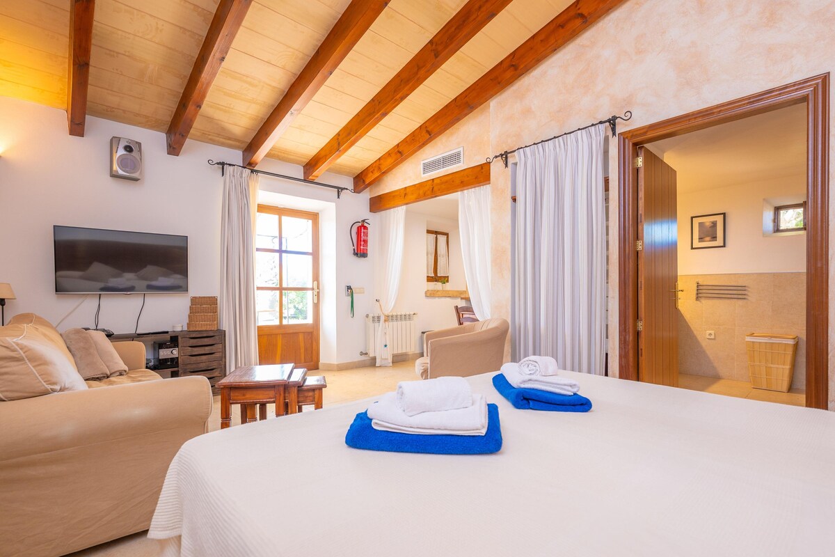 Habitación de hotel con cama, sofá, televisión y baño visible a través de una puerta abierta.