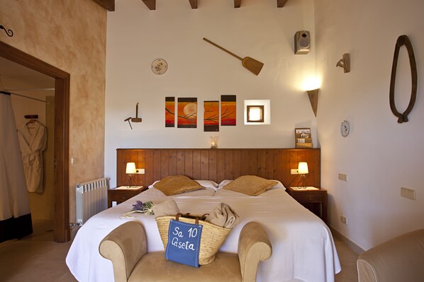 Una habitación de hotel con una cama grande, dos mesitas de noche con lámparas, un cabecero de madera, y una pared con una obra de arte y una lámpara colgante.