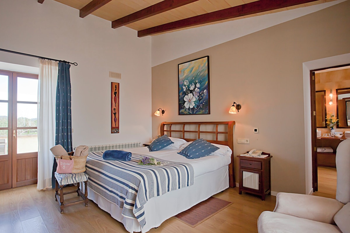 Un dormitorio con una cama grande, una silla, una mesita y una ventana con cortinas.