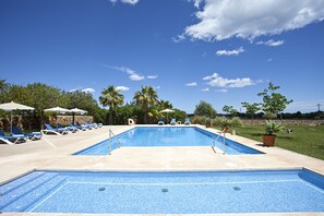 Piscina rectangular con solárium empedrado, rodeada de sillones de descanso y sombrillas.