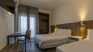 Une chambre d’hôtel avec deux lits, un bureau, une chaise, une armoire et une petite table.