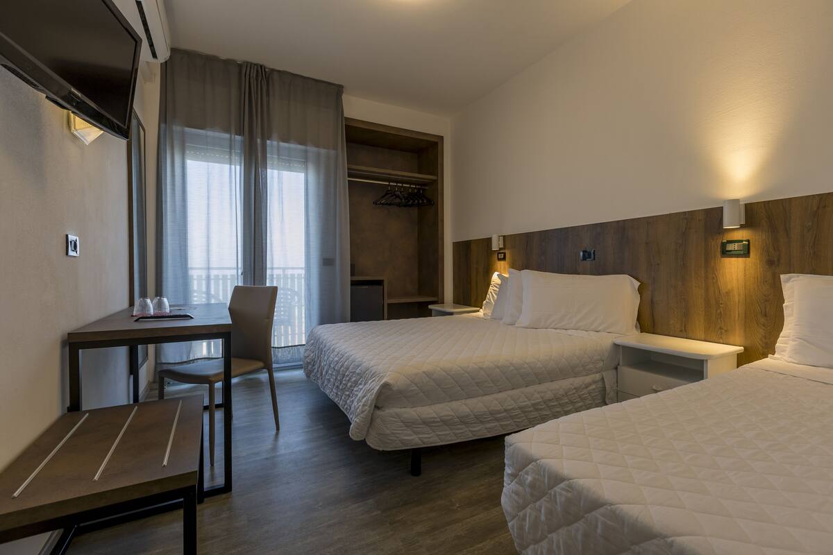 A hotel room with two beds, a desk, a chair, a wardrobe, and a small table.