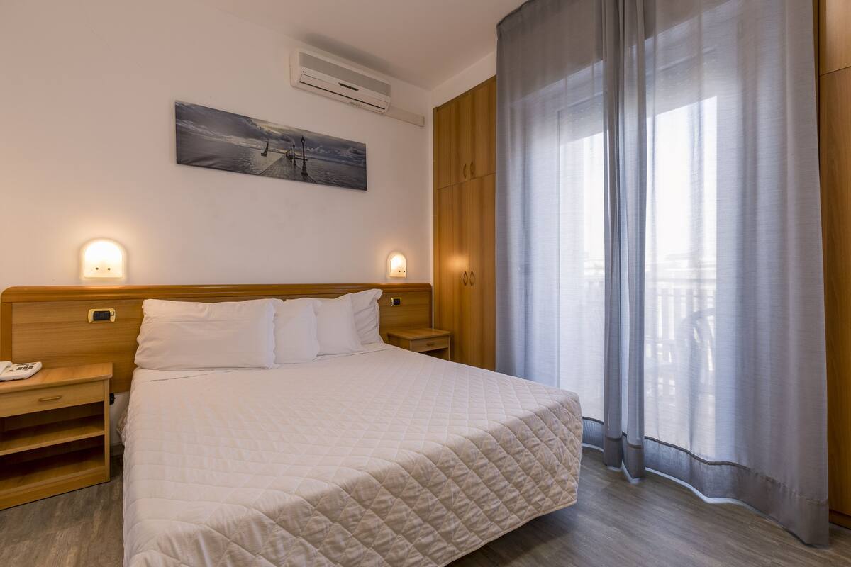 A neatly made bed with a quilted blanket, wooden headboard, bedside tables, and a wall-mounted air conditioner.