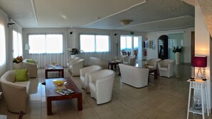 Un hall d’hôtel spacieux, doté d’un espace salon, d’un comptoir d’accueil et offrant une vue sur la mer.