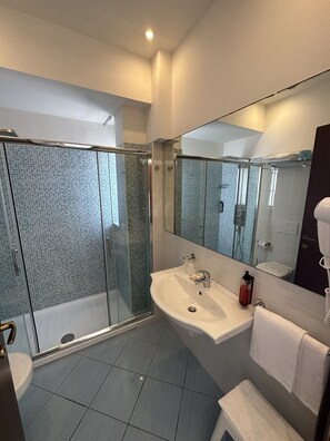 A modern bathroom with a glass-enclosed shower, a white sink, and a large mirror. - Hotel Centrale (Cervia)