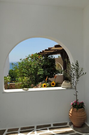 A white wall with a large arched window overlooking a garden with sunflowers and a view of the sea.