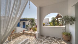 A balcony with a stone floor, white walls, and a view of a blue building. - Porto Vlastos (Tinos)