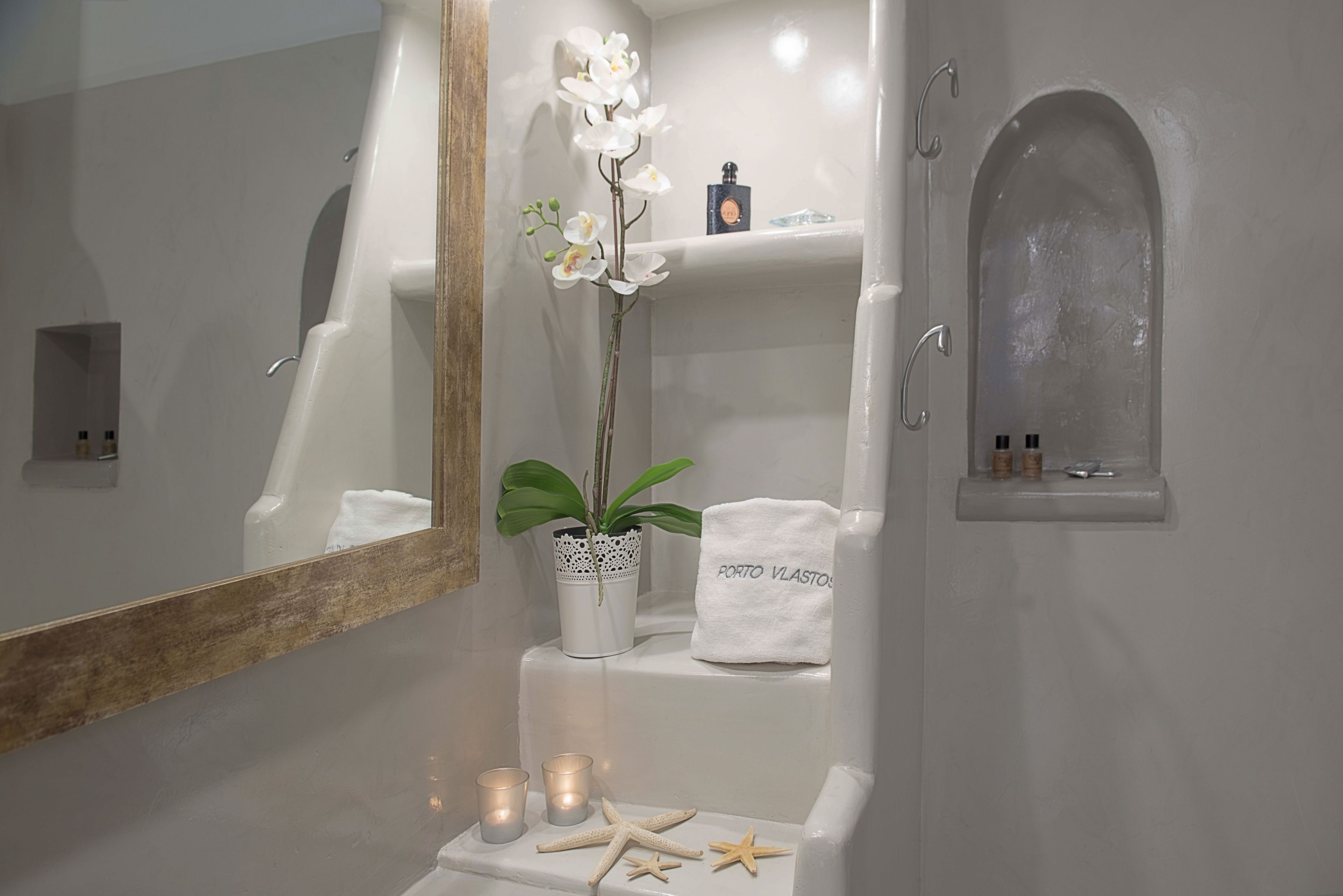 Une salle de bain avec une baignoire blanche, un miroir, une étagère avec des articles de toilette, une serviette et des objets décoratifs comme des bougies et des étoiles de mer.