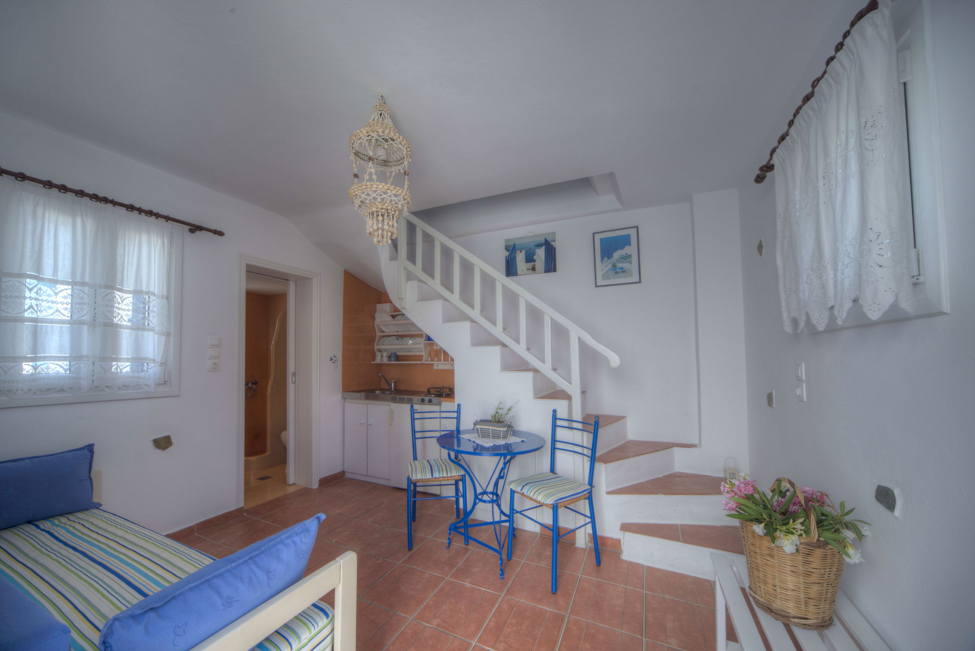 Un dormitorio con cama, ventana con cortinas, una escalera que lleva a una cocina y un comedor con sillas y una mesa.