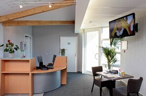 A reception area with a desk, chairs, a television, and a potted plant. - The Originals City, Hôtel Albizia,sarlat-la-canéda (Sarlat-la-Canéda)