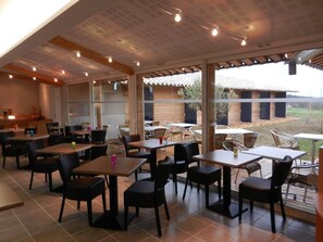A restaurant with indoor and outdoor seating, large windows, and a view of the outside. - The Originals City, Hôtel Albizia,sarlat-la-canéda (Sarlat-la-Canéda)