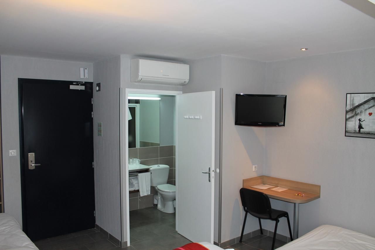 Habitación de hotel con cama, escritorio, silla, televisión y baño visible a través de una puerta abierta.