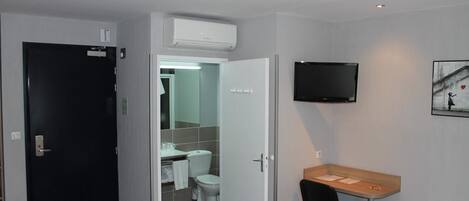 Habitación de hotel con cama, escritorio, silla, televisión y baño visible a través de una puerta abierta.