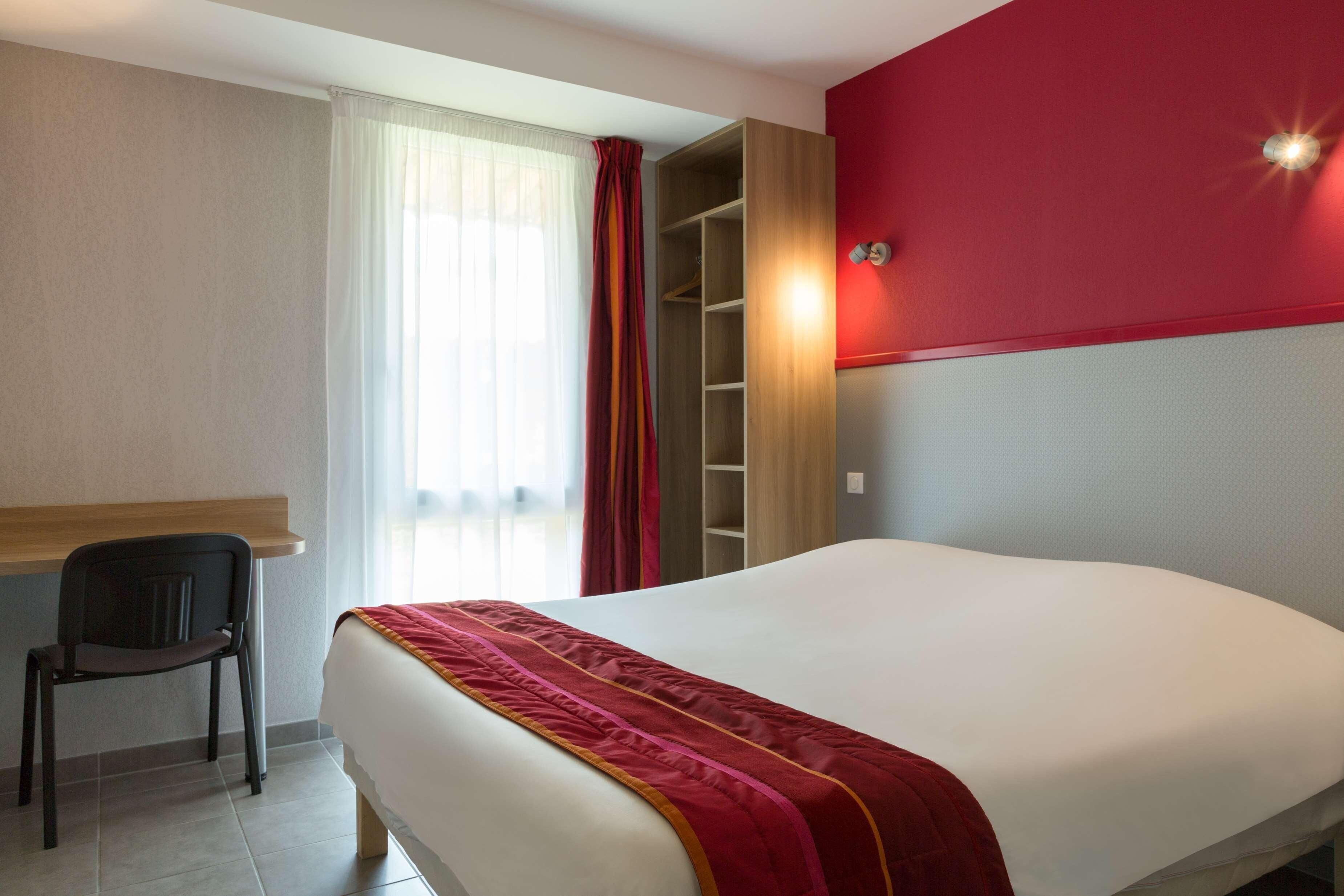 A hotel room with a bed, a chair, a wardrobe, and a window with curtains.