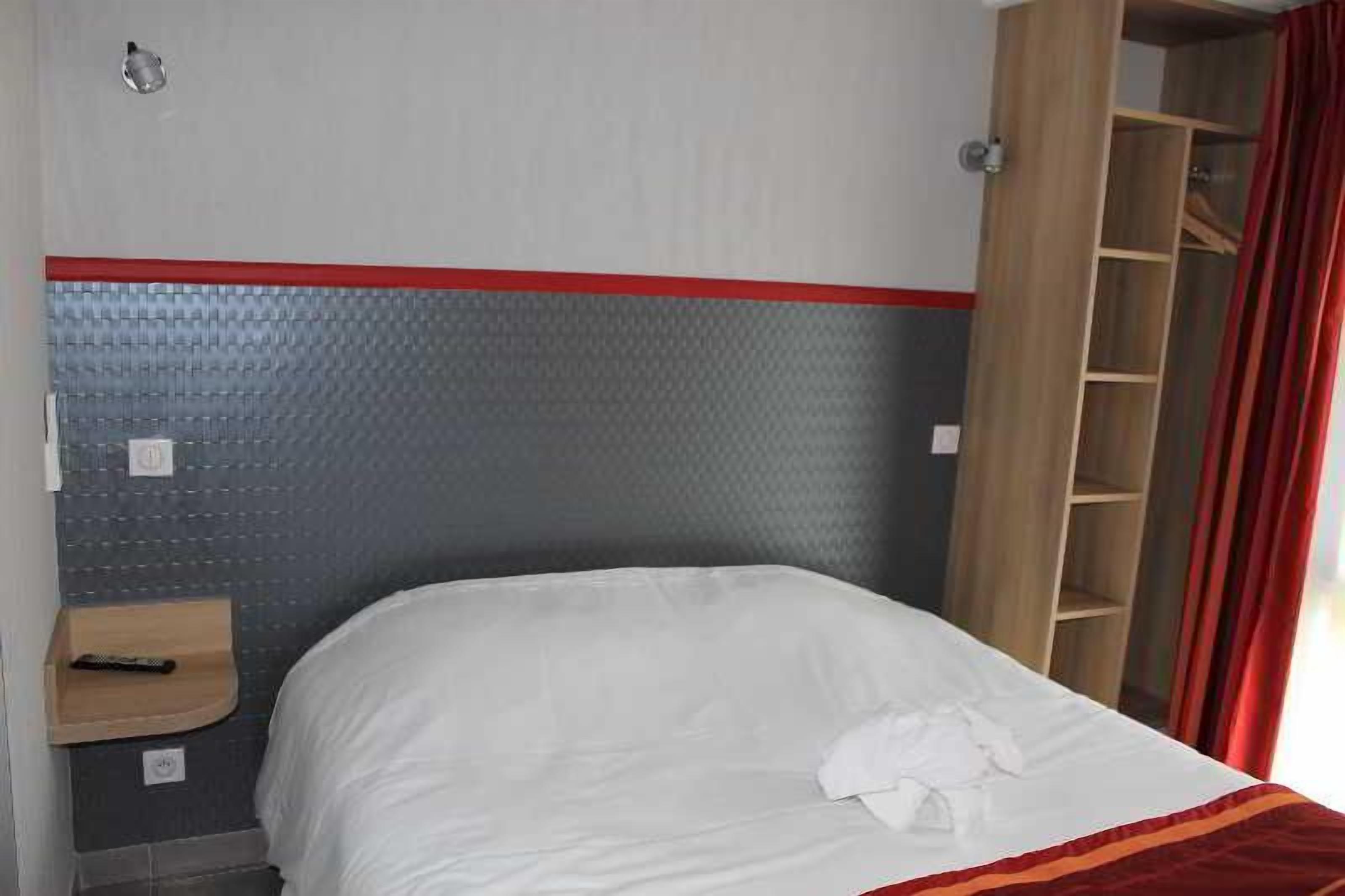 A hotel room with a bed, a wooden nightstand, a red-striped headboard, and a wardrobe with a red curtain.