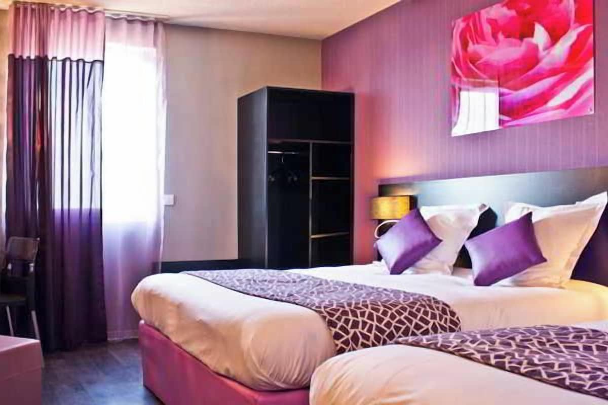 A hotel room with a large bed, a bedside table, a chair, a wardrobe, and a painting on the wall.