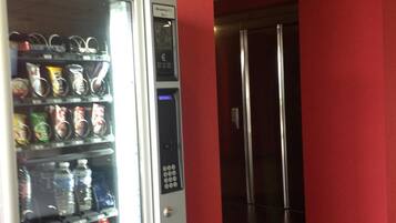 A vending machine with various snacks and drinks, a control panel, and a red wall.