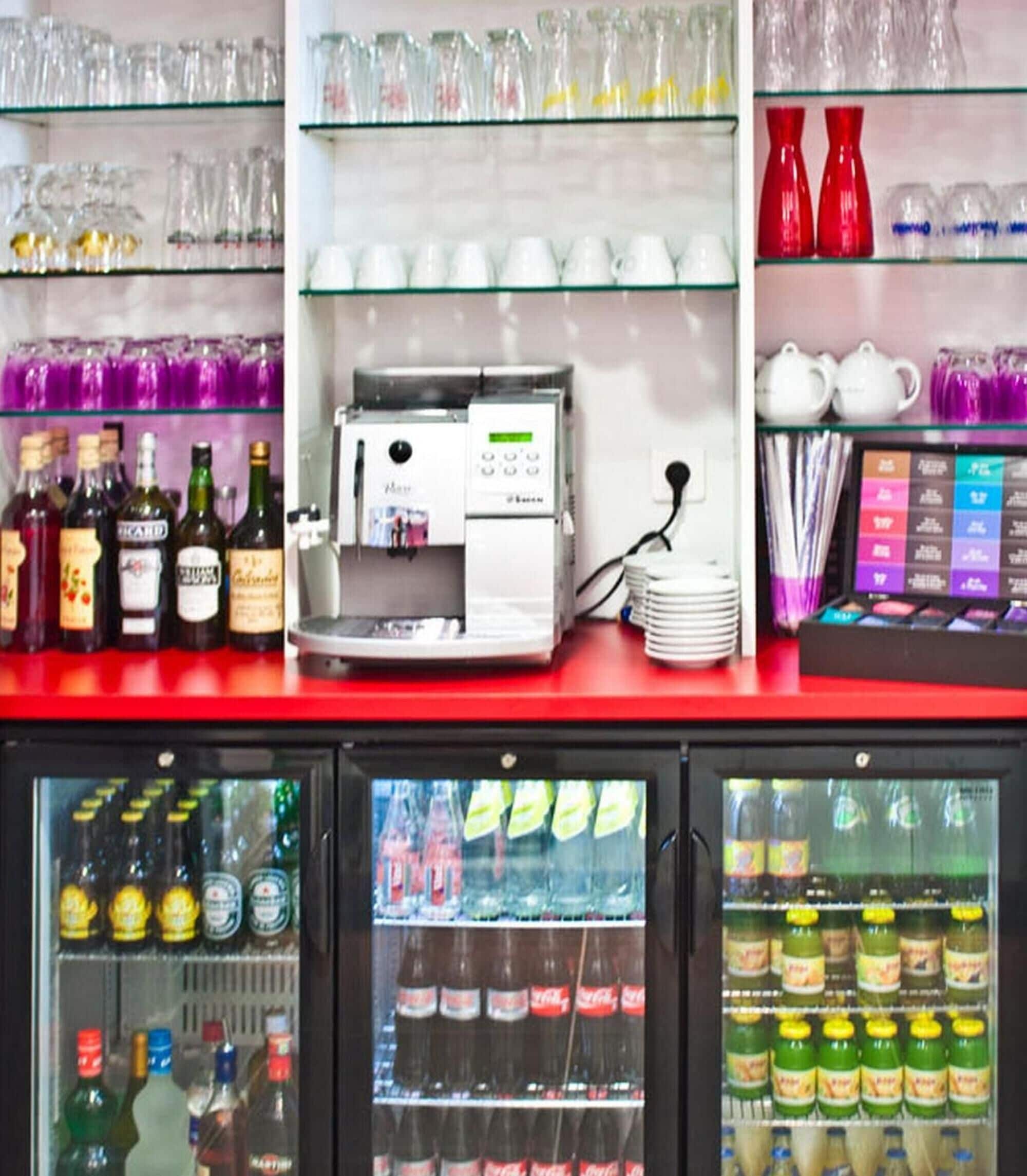 A beverage vending machine with a coffee dispenser, surrounded by shelves of bottled drinks and glassware.