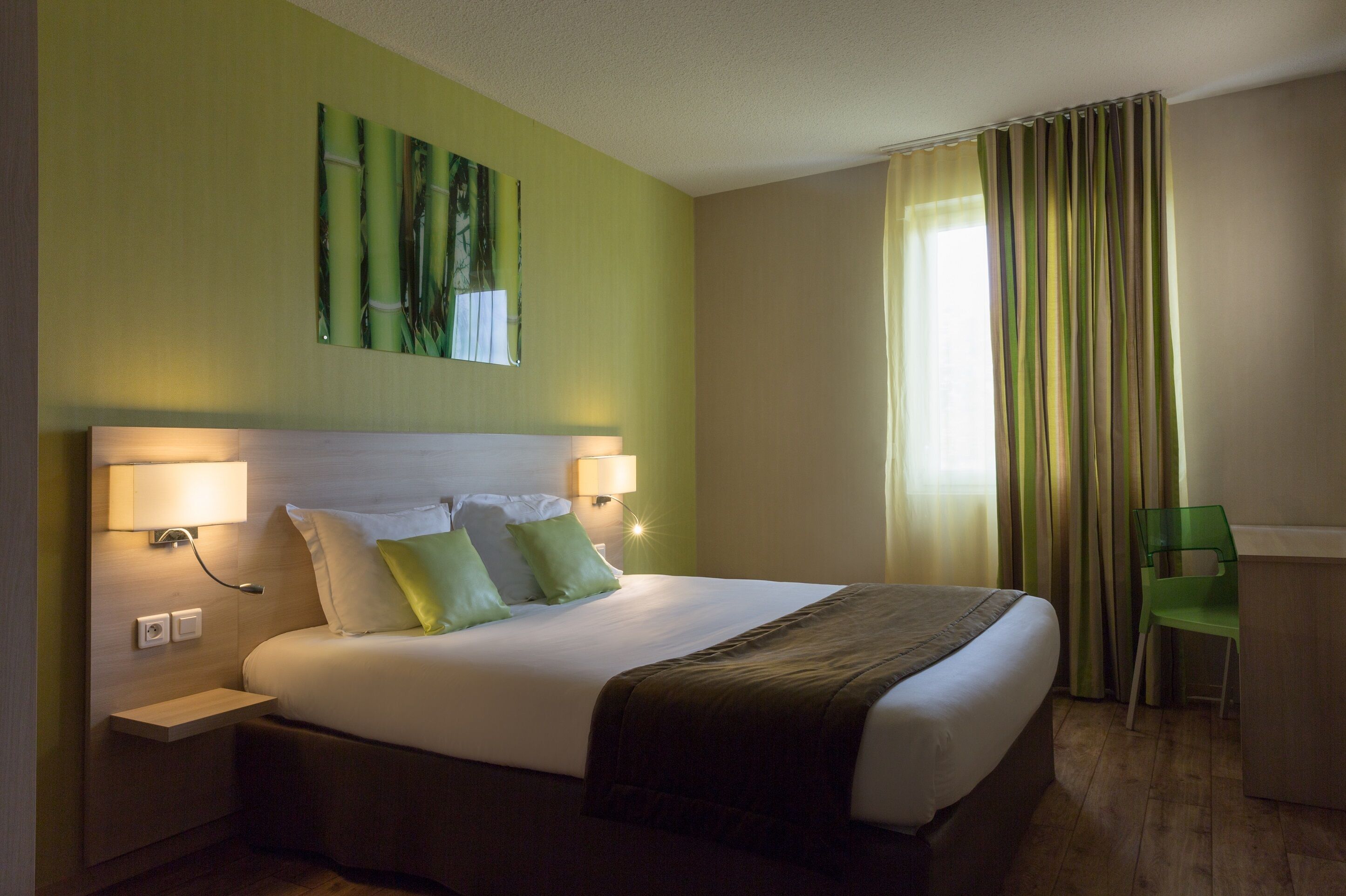 Una habitación de hotel con una cama grande, dos lámparas de noche, una silla verde y un escritorio.