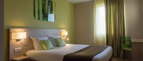 Een hotelkamer met een groot bed, twee bedlampjes, een groene stoel en een bureau.