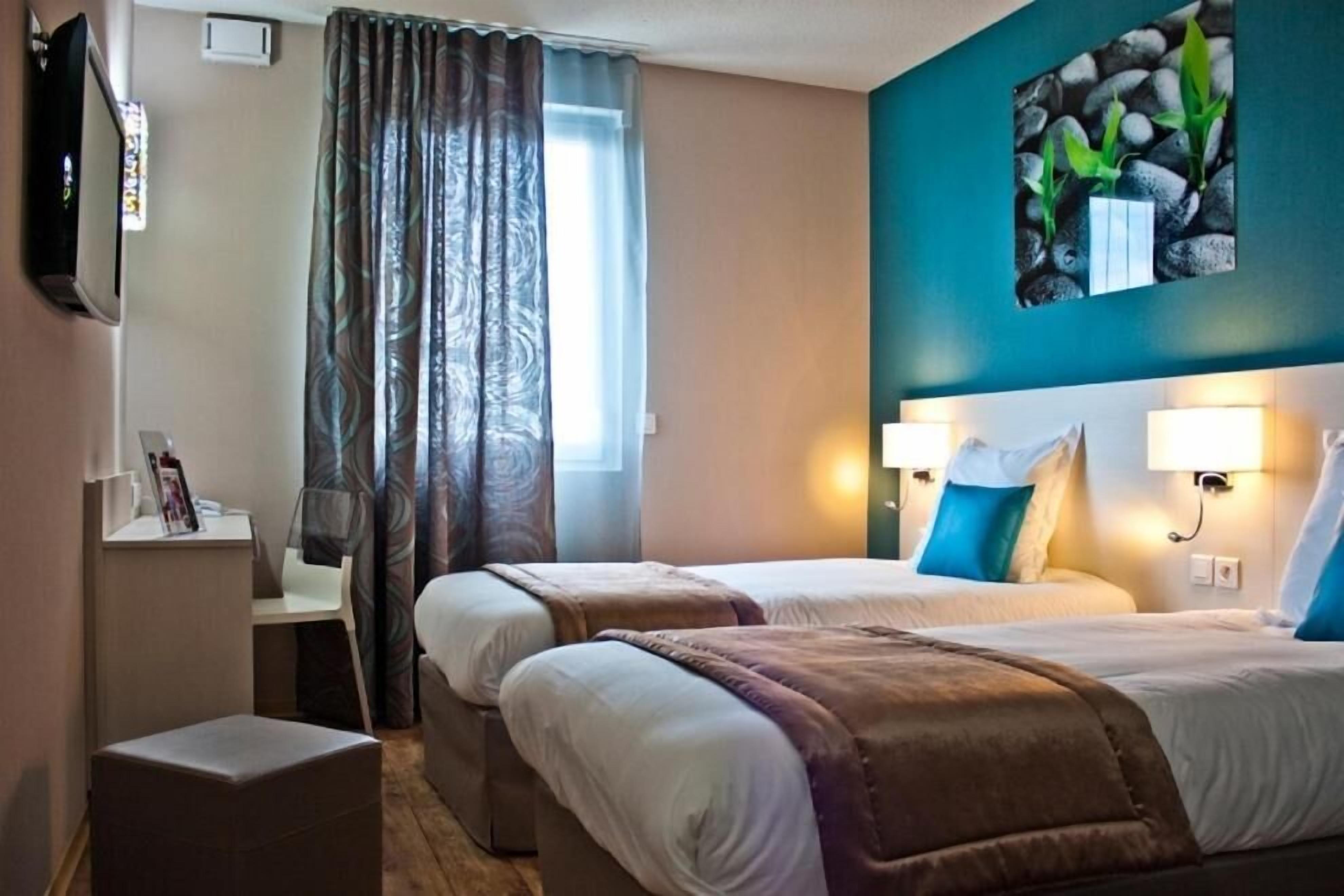 Una habitación de hotel con dos camas, televisión, escritorio y ventana con cortinas.