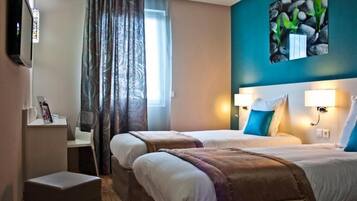 Una habitación de hotel con dos camas, televisión, escritorio y ventana con cortinas.