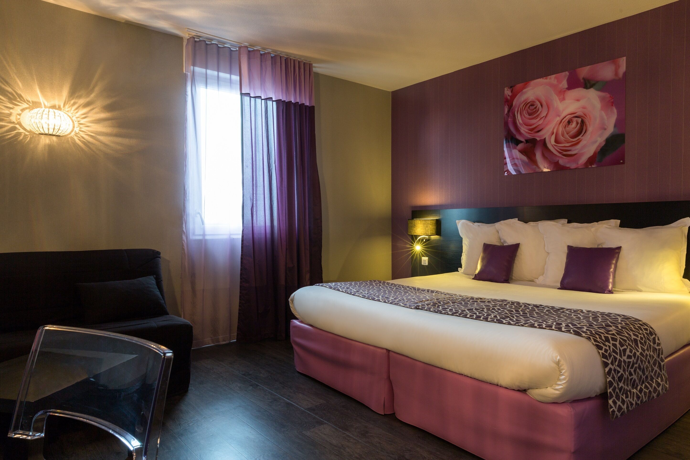 Habitación de hotel con una cama grande, un sofá, una mesita de vidrio y una lámpara de pared.