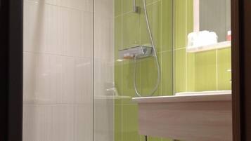 Une douche avec une porte en verre, un mur recouvert de carreaux verts, une baignoire blanche et un lavabo avec un miroir au-dessus.