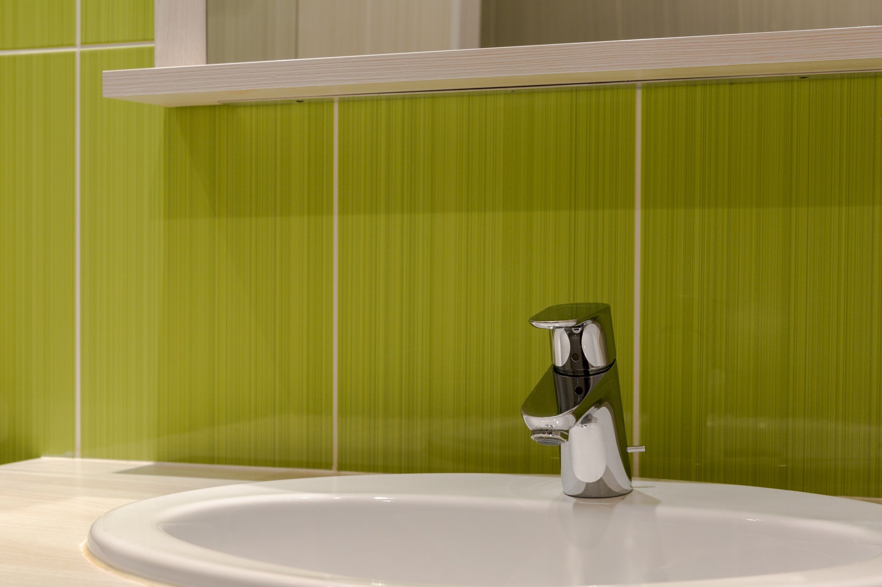 A bathroom with a white sink and a chrome faucet against a green tiled wall.