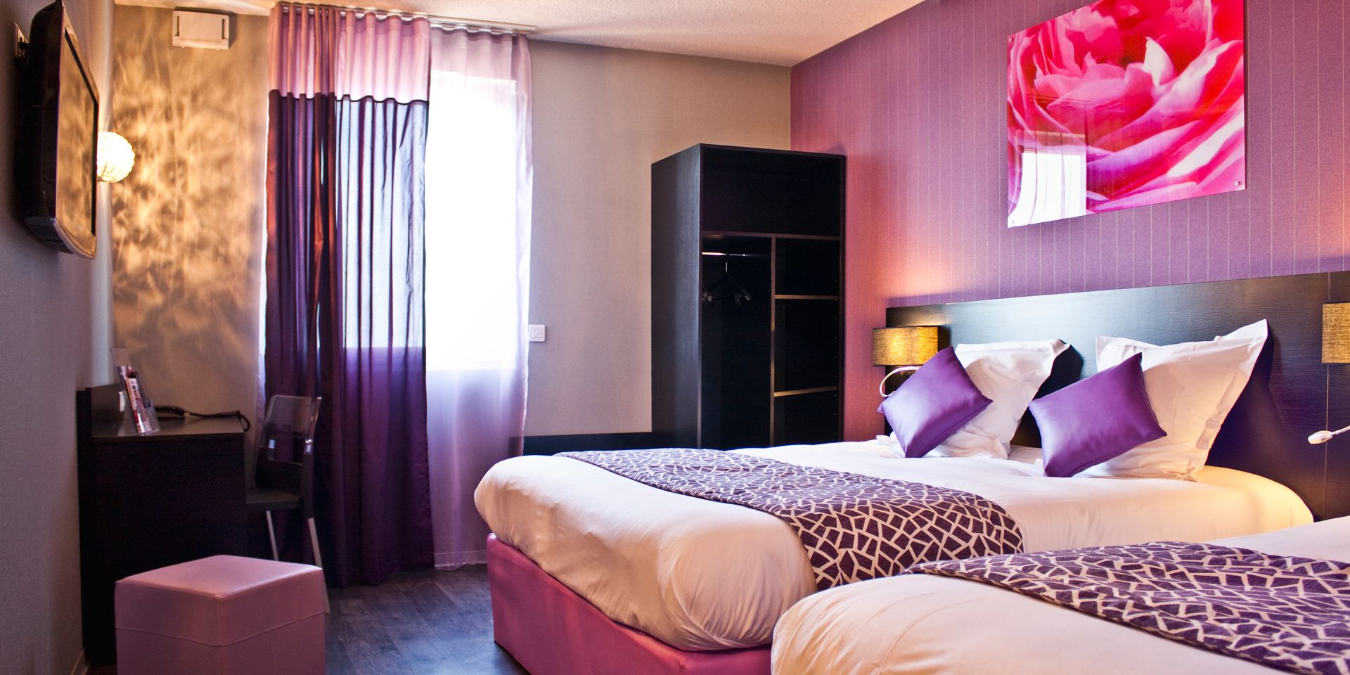 Habitación de hotel con dos camas, un armario, un escritorio y un amplio ventanal con cortinas.