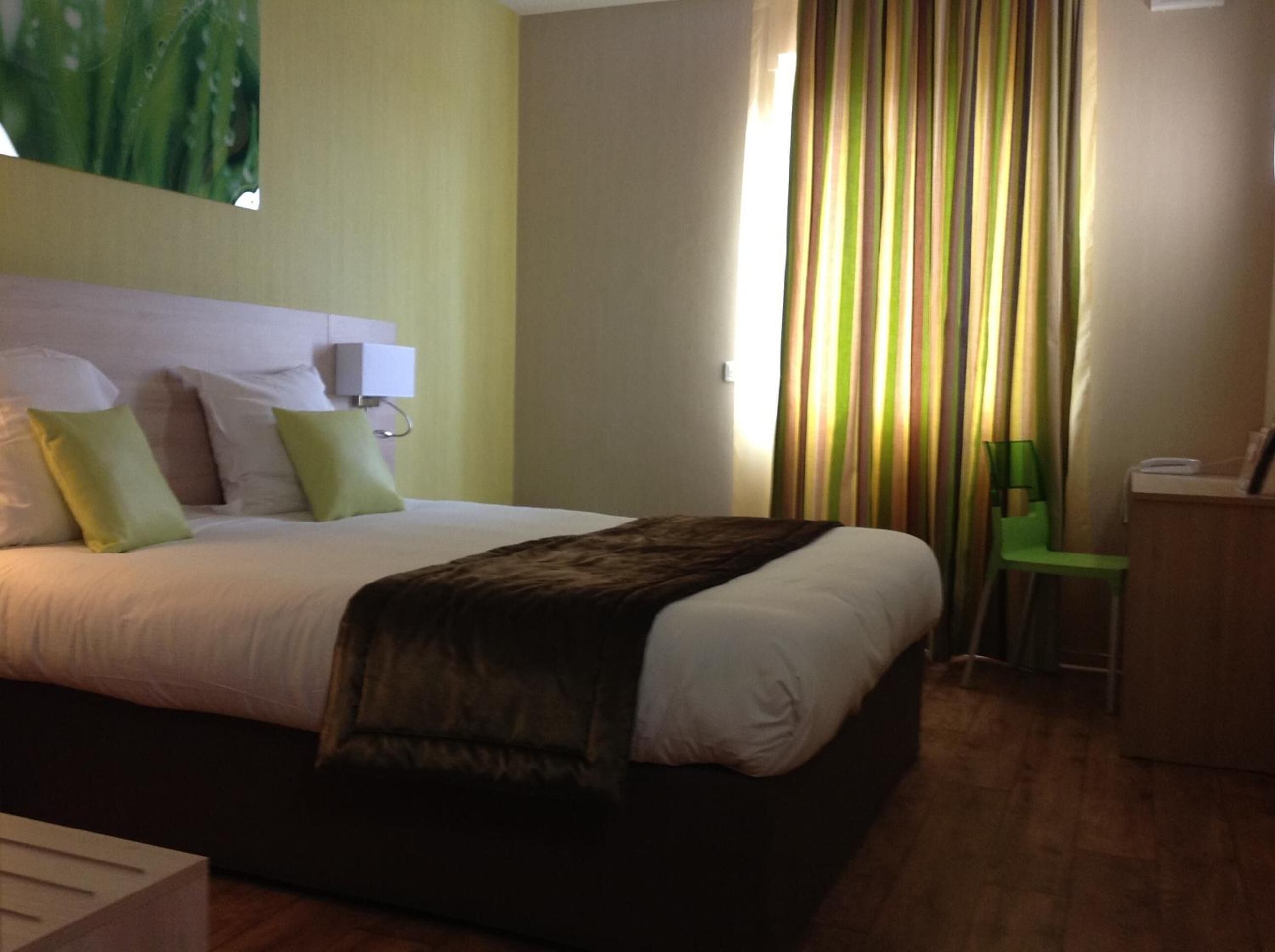 Una habitación de hotel con cama, escritorio, lámpara y cortina.
