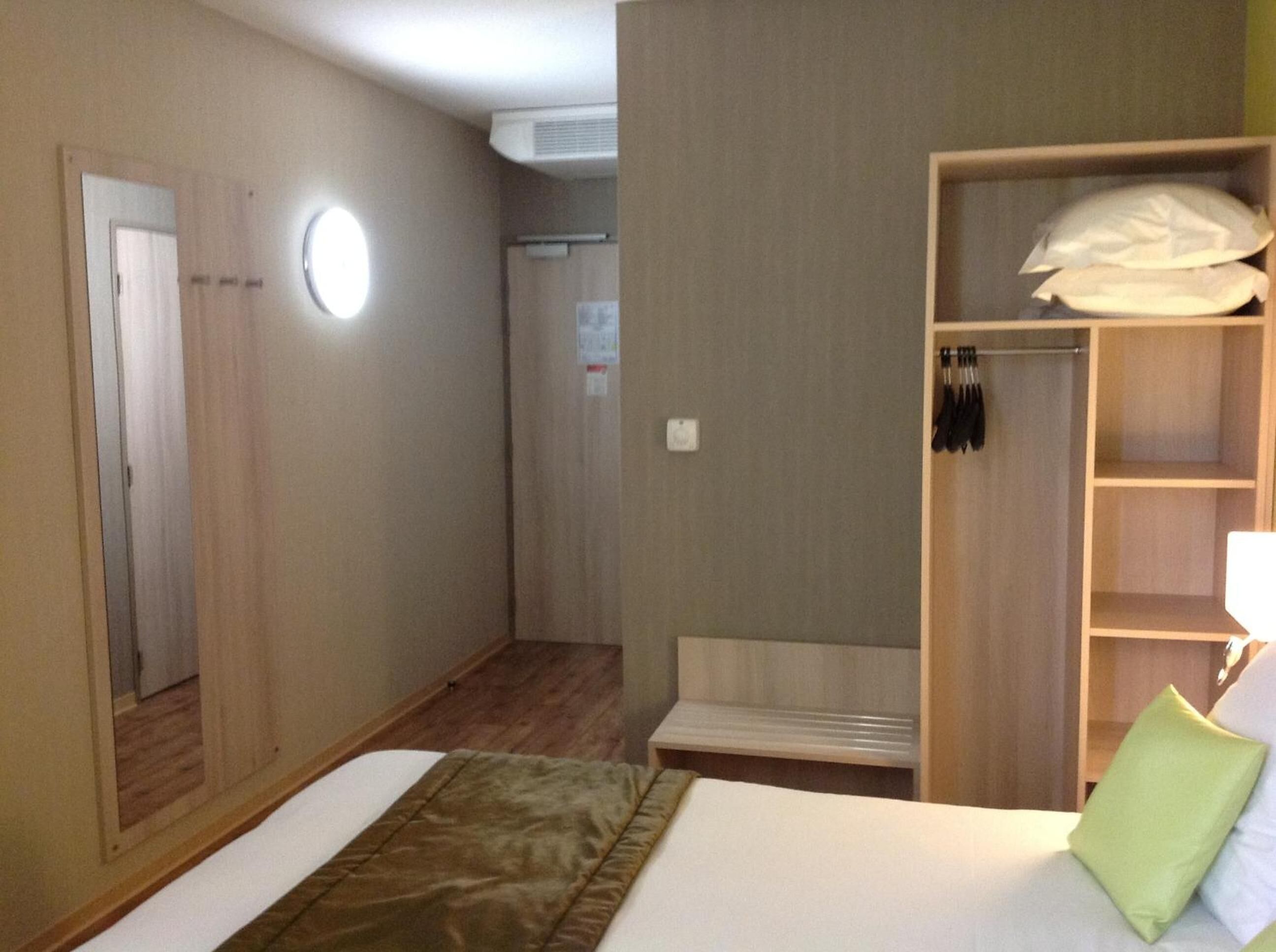 Una habitación de hotel con cama, armario, espejo y zona de ducha.