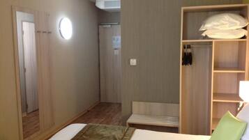 Una habitación de hotel con cama, armario, espejo y zona de ducha.