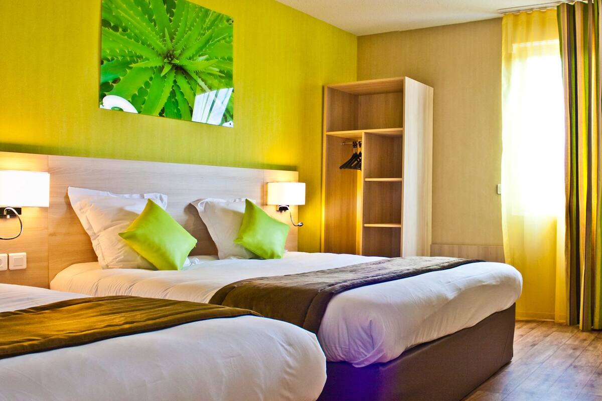 Une chambre d’hôtel avec deux lits, une armoire, un bureau et une chaise verte.