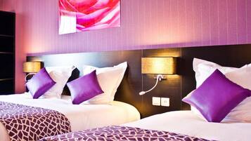 A hotel room with two beds, each with white linens and purple pillows. There are wall-mounted lamps on either side of the beds.