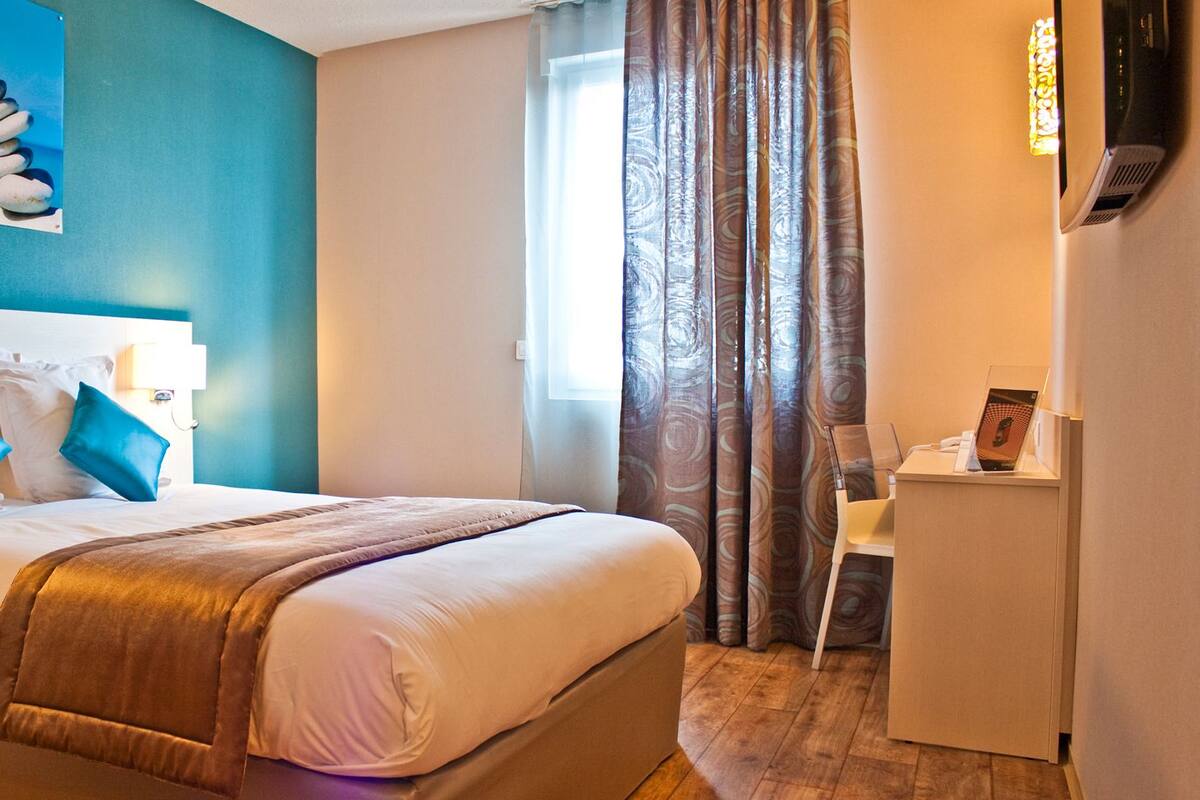 Une chambre d’hôtel équipée d’un lit, d’un bureau, d’une chaise et d’un téléviseur fixé au mur.