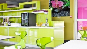 Un'area cucina luminosa e colorata con mobili verdi, un frigorifero nero e un lavandino. Sono presenti due sedie verdi e un tavolo.