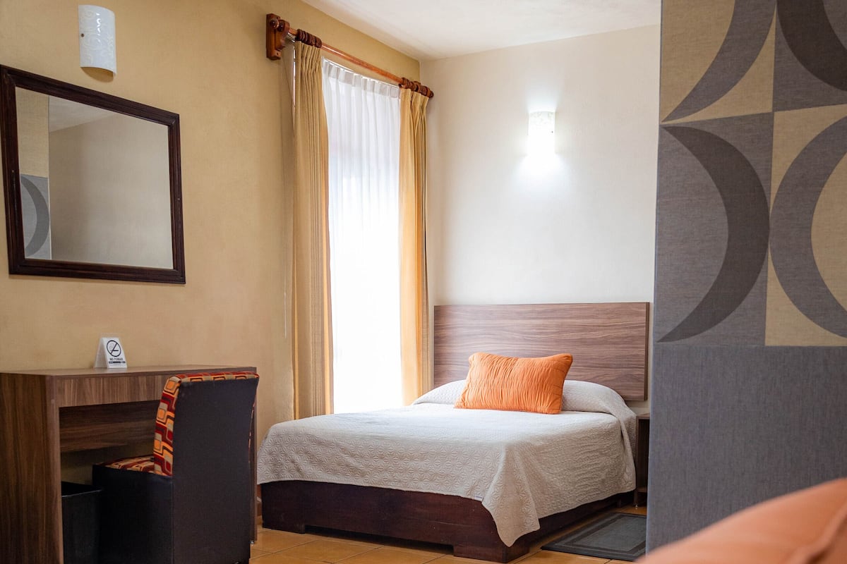 A hotel room with two beds, a desk, a mirror, and a window with curtains.
